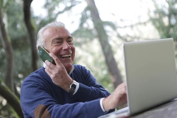 homem sorrindo mexendo no computador e falando no celular